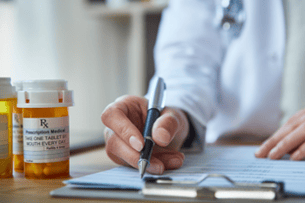 Clinician reviews clipboard notes related to a bottle of prescription pills in the foreground