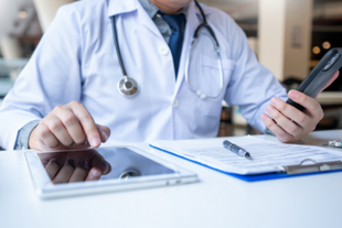 Physician holding a phone while typing on an iPad