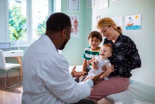 Pediatrician speaks to mom, who is holding a baby, while toddler son watches