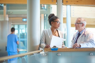 Male clinician and female executive chat in hospital hallway