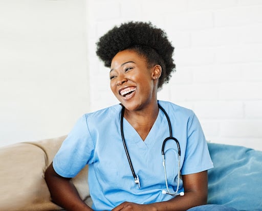 A nurse practitioner smiles in a brightly lit room on a couch